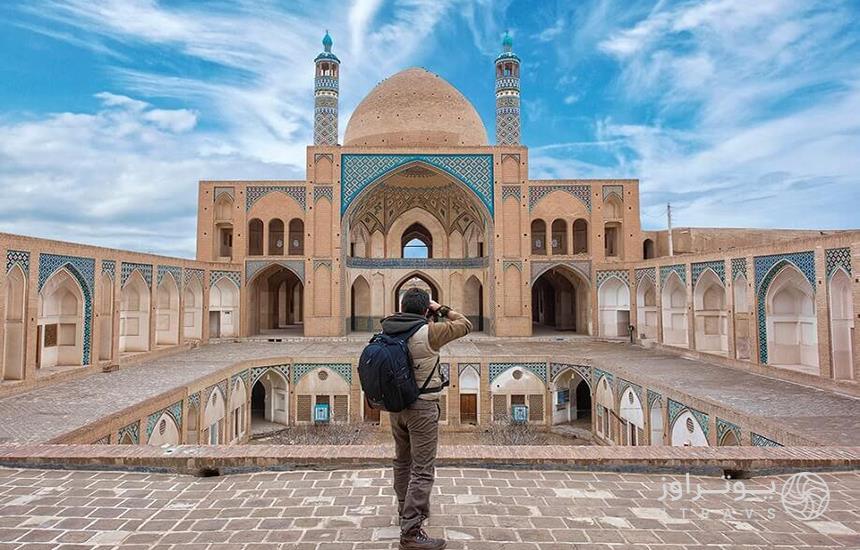 مردی درحال عکاسی با دوربین از مسجدی تاریخی در ایران